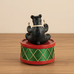 Black bear figurine on a green and red drum with gold accents on a white background