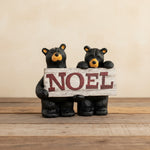 Two bear figurines holding a 'NOEL' sign on a white background