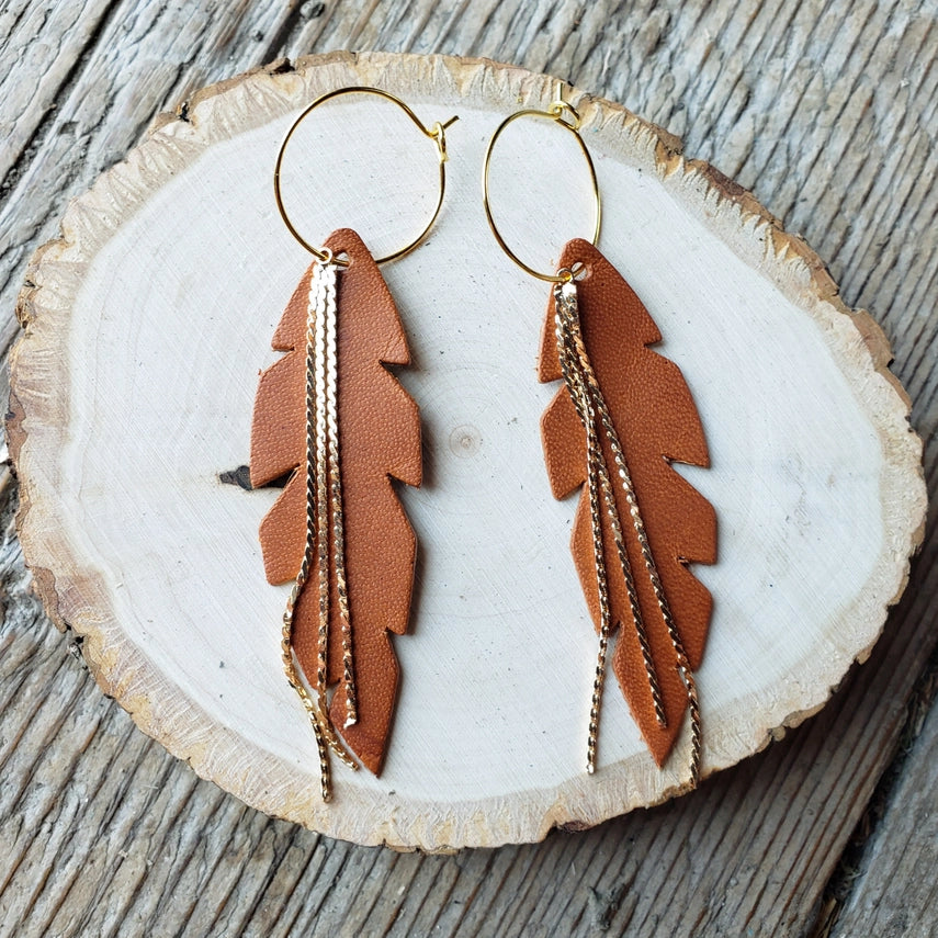 Feather-shaped earrings with gold chains on a wooden surface