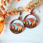 Pair of earrings with mountain design on a white surface with flowers.