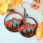 Pair of earrings with nature-themed design on a light blue background with flowers.