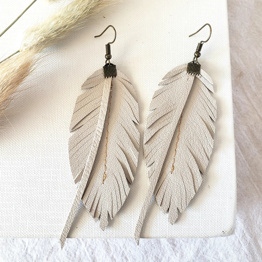 Feather-shaped earrings on a textured white surface