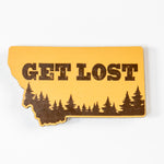 Yellow magnet shaped like the state of Montana with 'GET LOST' text and forest design on a white background