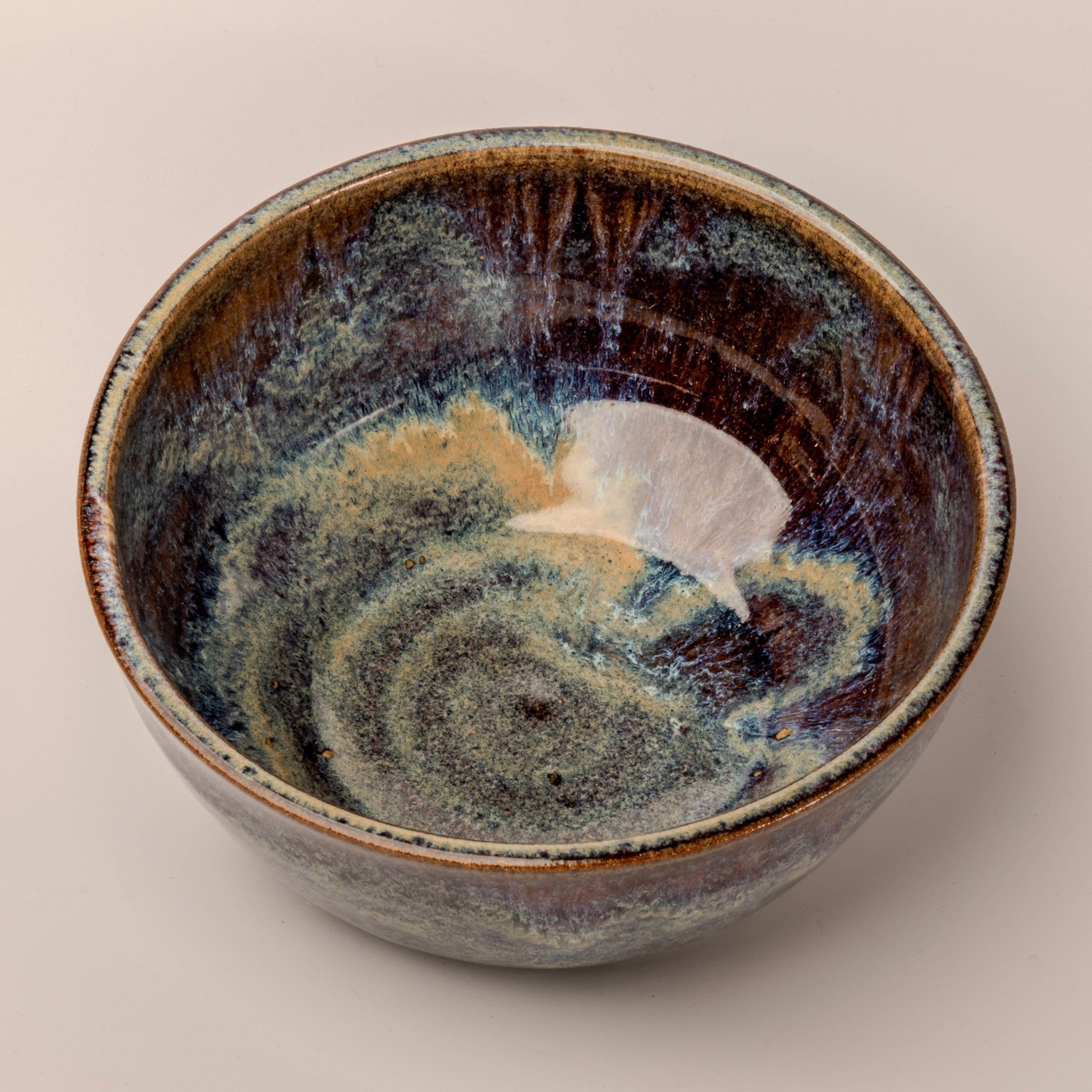 Stoneware bowl with a unique glaze pattern on a beige background