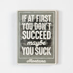 Motivational magnet with text 'If at first you don't succeed, maybe you suck. Montana' on a textured background.
