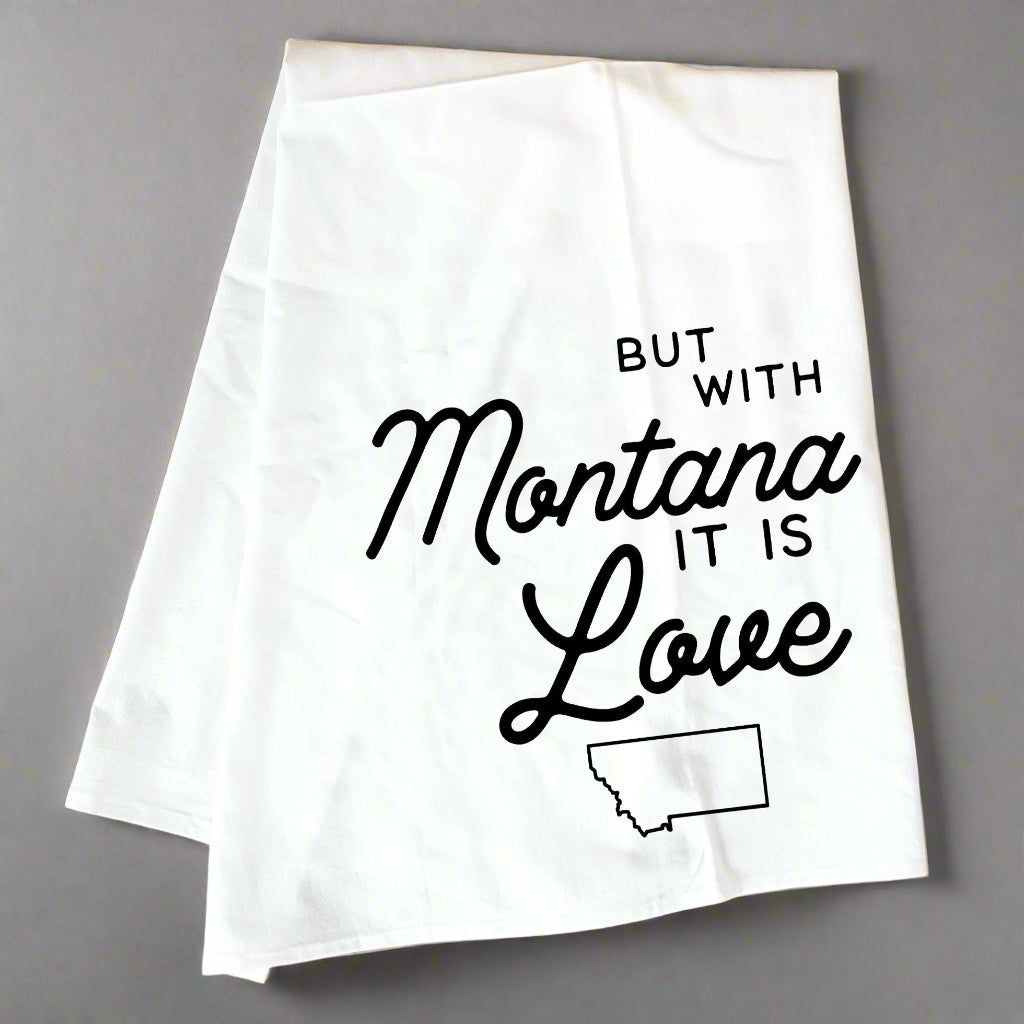 White towel with black text 'But with Montana it is Love' on a wooden surface