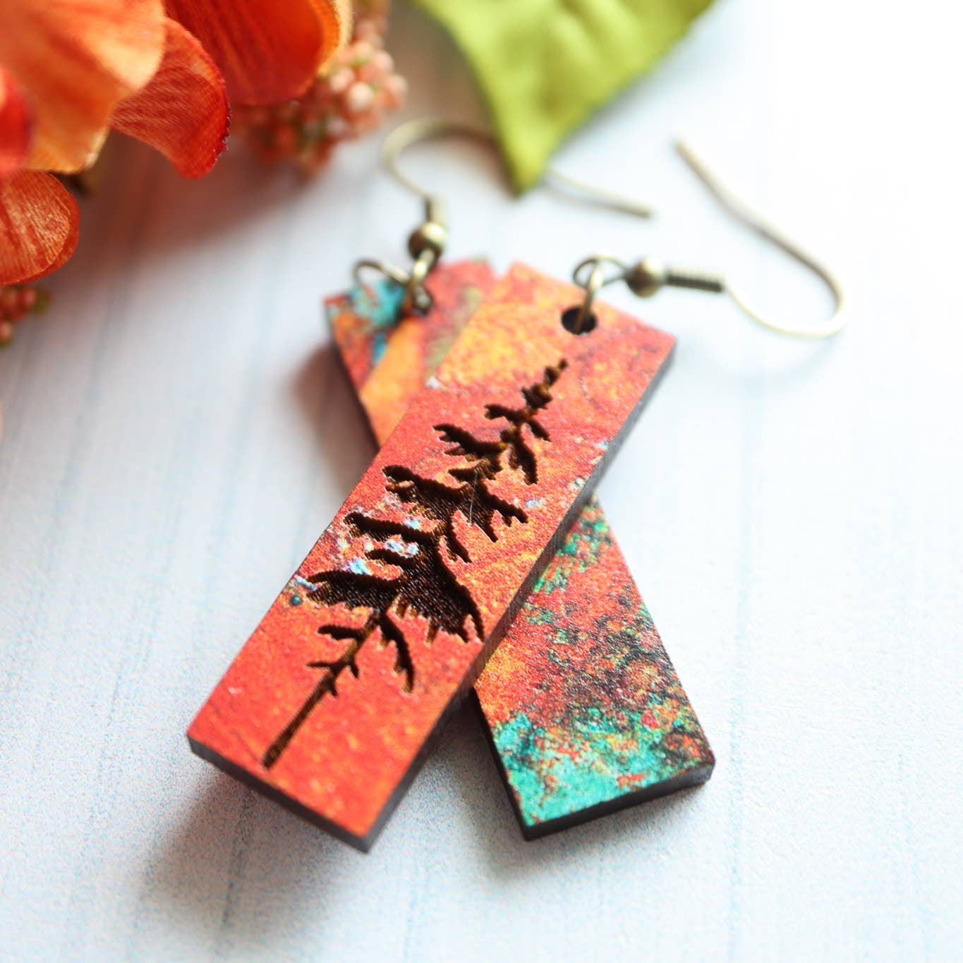 Colorful earrings with a tree design on a white surface with flowers in the background