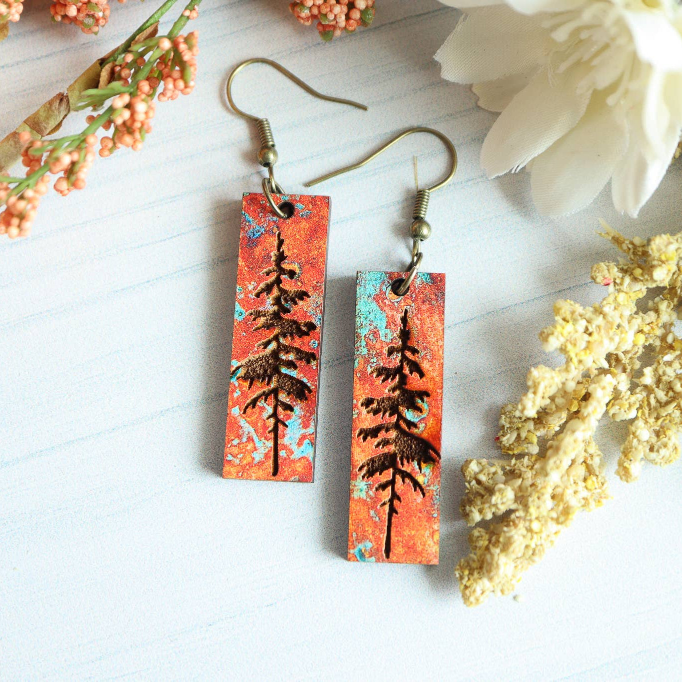 Pair of earrings with tree design on a white surface with flowers