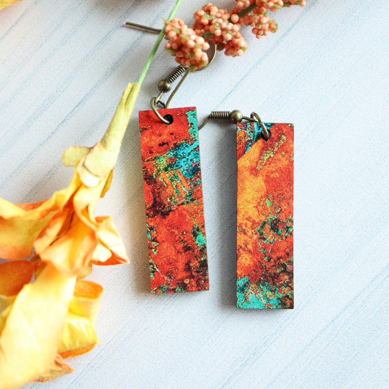 Colorful marbled earrings on a white surface with yellow flowers.