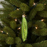 Green glass ornament shaped like a pickle spear on a white background