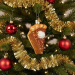 Glass ornament shaped like a slice of pie with whipped cream on a white background