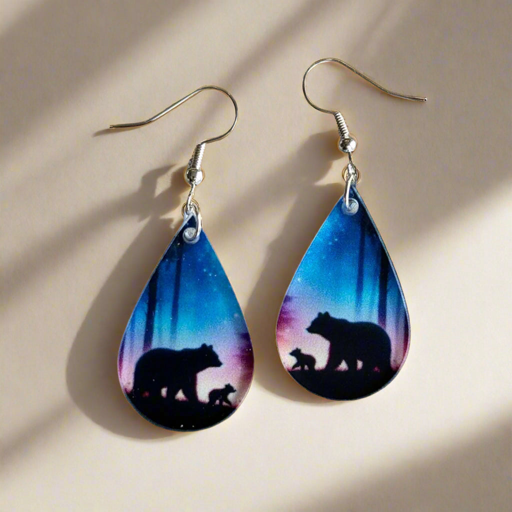 Teardrop-shaped earrings with bear silhouettes against a colorful background on a wooden surface.