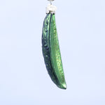 Green glass ornament shaped like a pickle spear on a white background