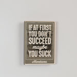 Motivational magnet with text 'If at first you don't succeed, maybe you suck. Montana' on a textured background.