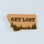 Yellow magnet shaped like the state of Montana with 'GET LOST' text and forest design on a white background