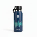 A Hydro Flask insulated water bottle in dark blue with a white forest tree graphic and the Hydro Flask logo, sitting on a wooden table with its box in the background.