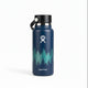 A Hydro Flask insulated water bottle in dark blue with a white forest tree graphic and the Hydro Flask logo, sitting on a wooden table with its box in the background.