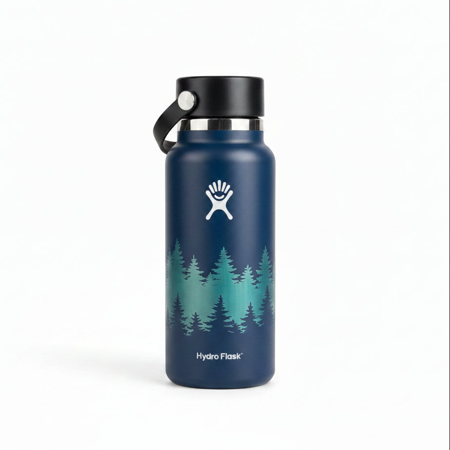 A Hydro Flask insulated water bottle in dark blue with a white forest tree graphic and the Hydro Flask logo, sitting on a wooden table with its box in the background.