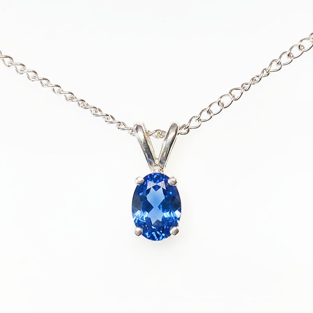 A silver chain necklace with a oval-cut blue gemstone pendant in a silver setting, shown against a plain white background.