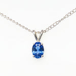 A silver chain necklace with a oval-cut blue gemstone pendant in a silver setting, shown against a plain white background.