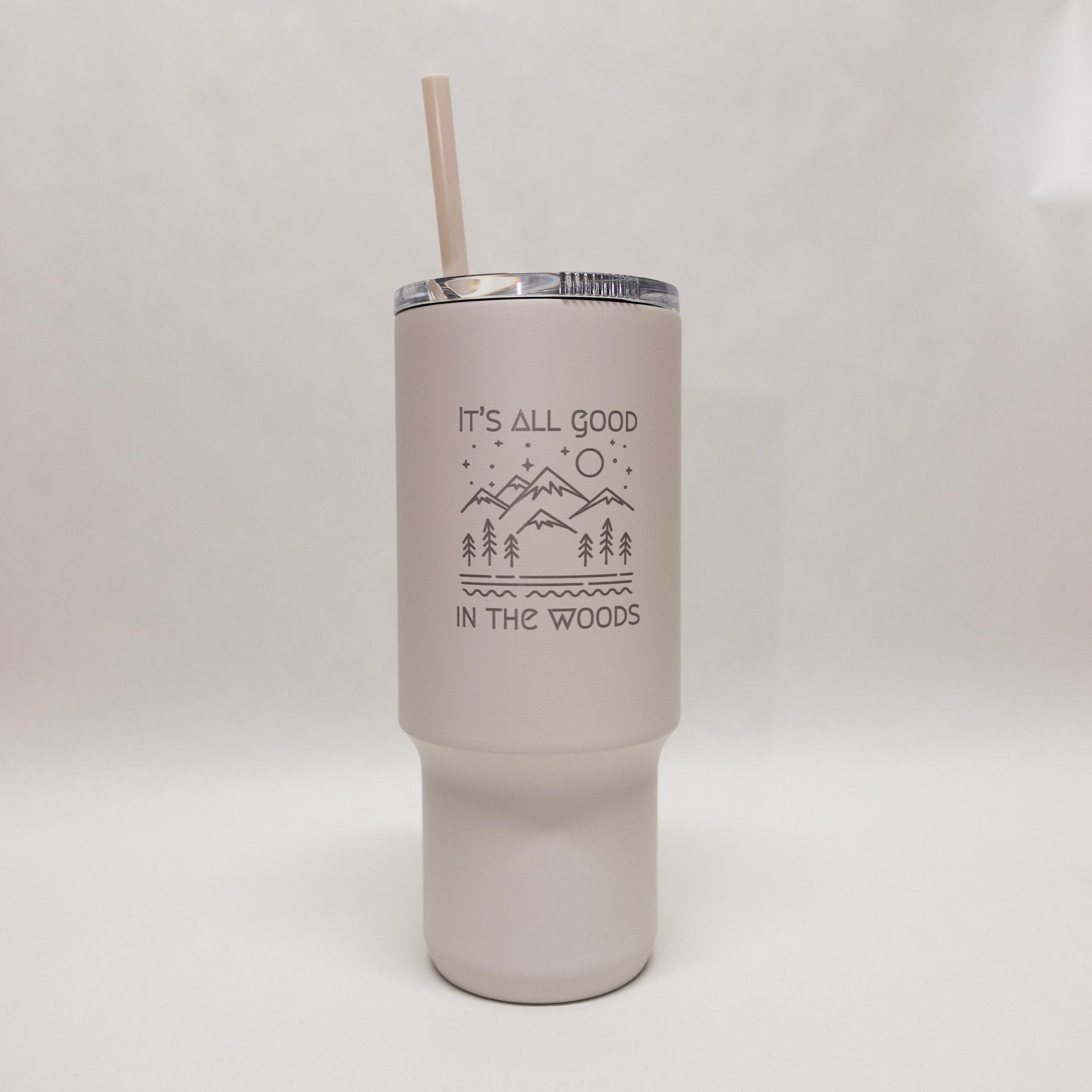 White tumbler with an engraved design with mountains and trees and the words "It's all good in the woods"