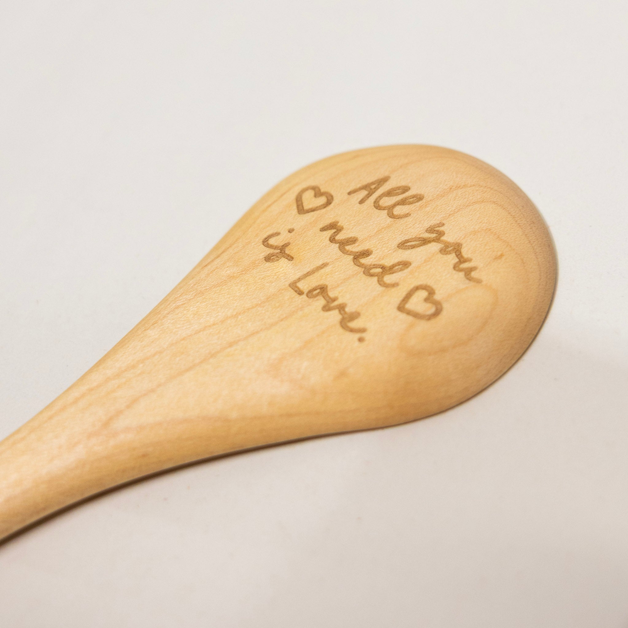 Wooden spoon with engraved text 'All you need is love' on a light background