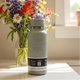 Light gray insulated bottle with floral arrangement in the background