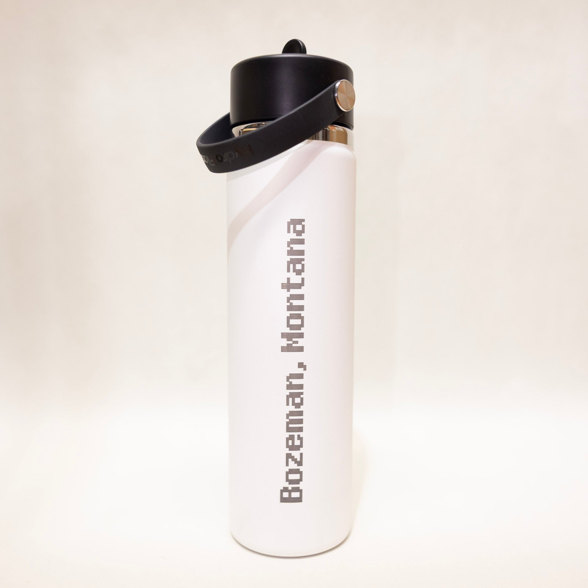 White water bottle with black cap and 'Bozeman, Montana' text on a light beige background