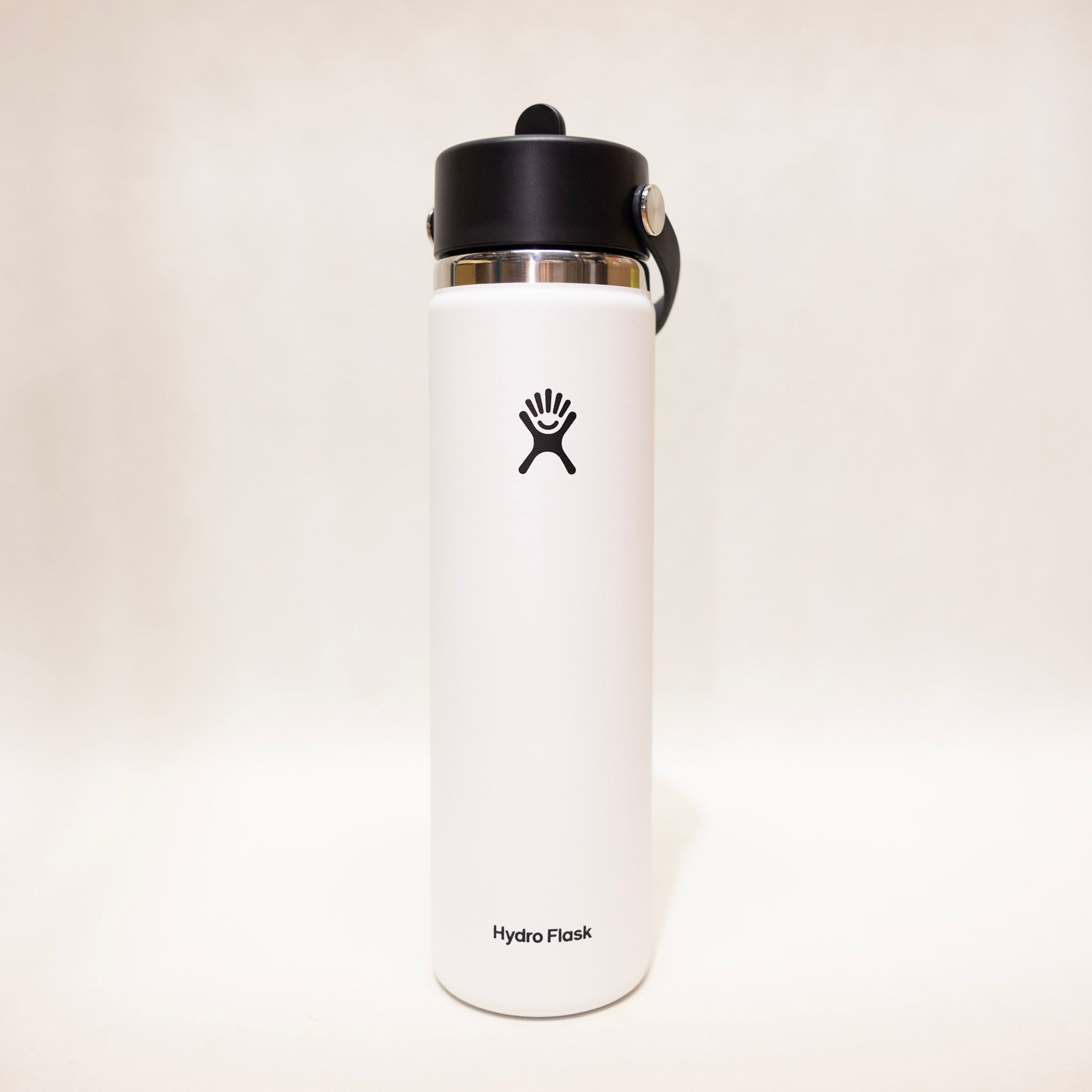 White Hydro Flask water bottle with black lid on a light beige background