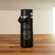 Black insulated bottle with mountain and coffee design on a wooden surface