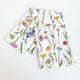 A folded white fabric napkin or tea towel with a colorful wildflower print, displayed on a white-washed wooden surface.
