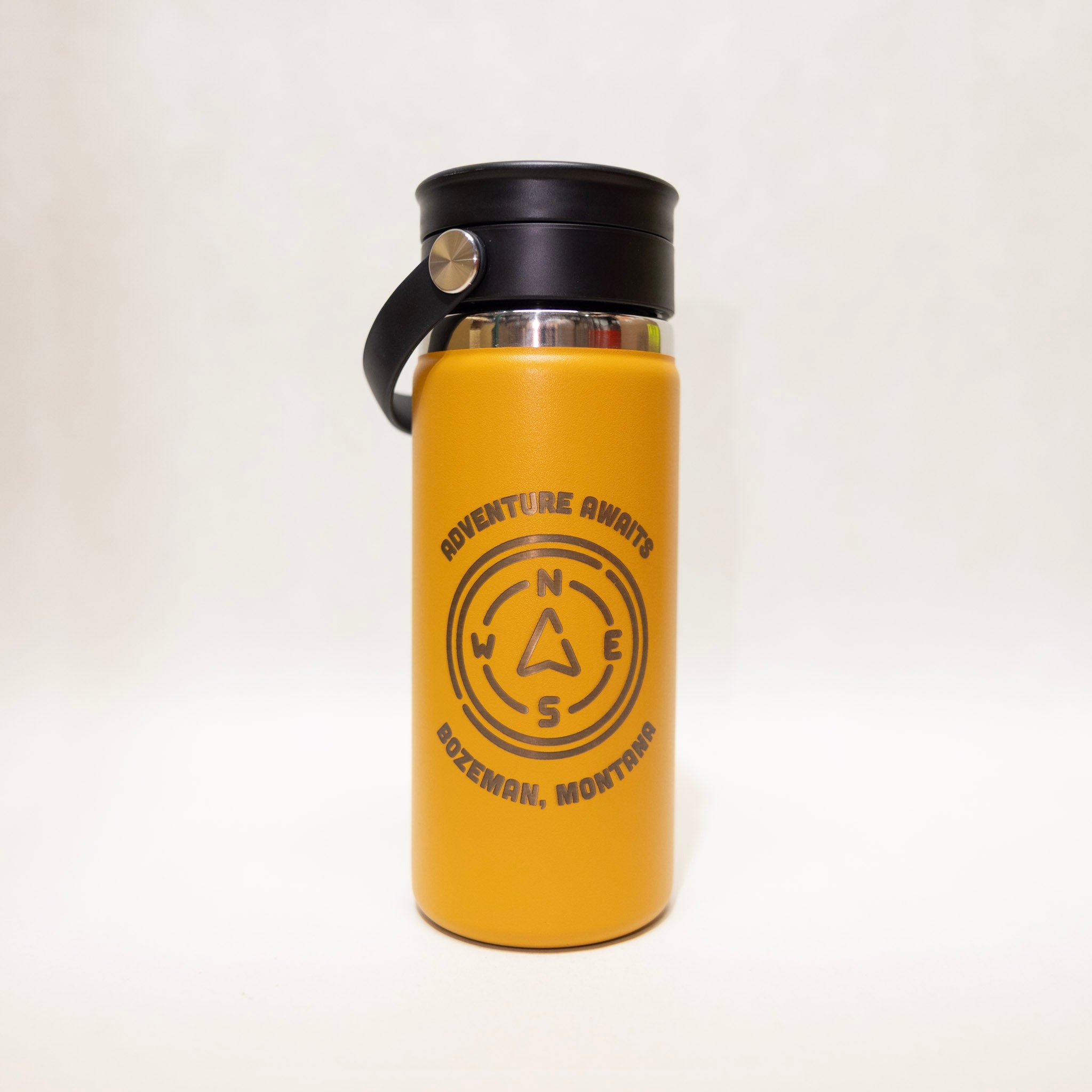 Yellow water bottle with black lid and 'Adventure Awaits' text on a white background