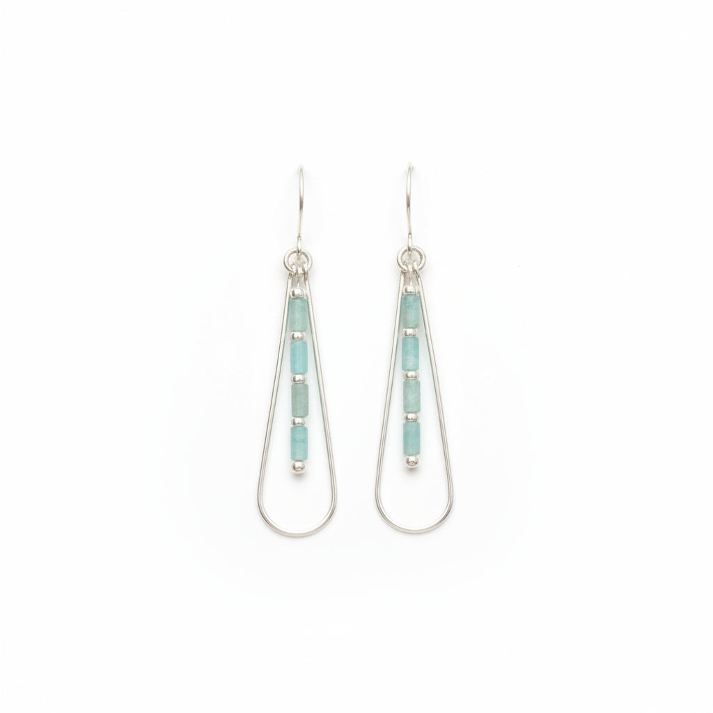A pair of silver drop earrings with vertical rows of light blue-green rectangular beads, displayed on a textured off-white surface.