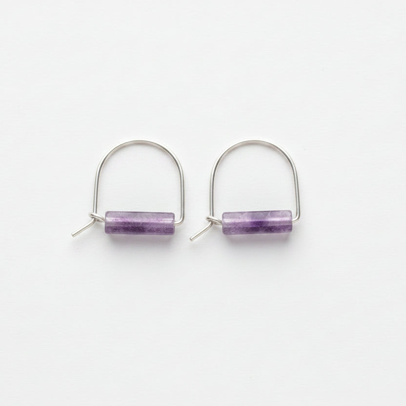 A pair of silver hoop earrings with a small rectangular purple amethyst stone in the center, displayed on a white surface