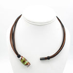 A multi-strand necklace with dark brown and black cords, featuring a large cylindrical glass lampwork bead with green, brown, and white patterns, displayed on a white mannequin bust.