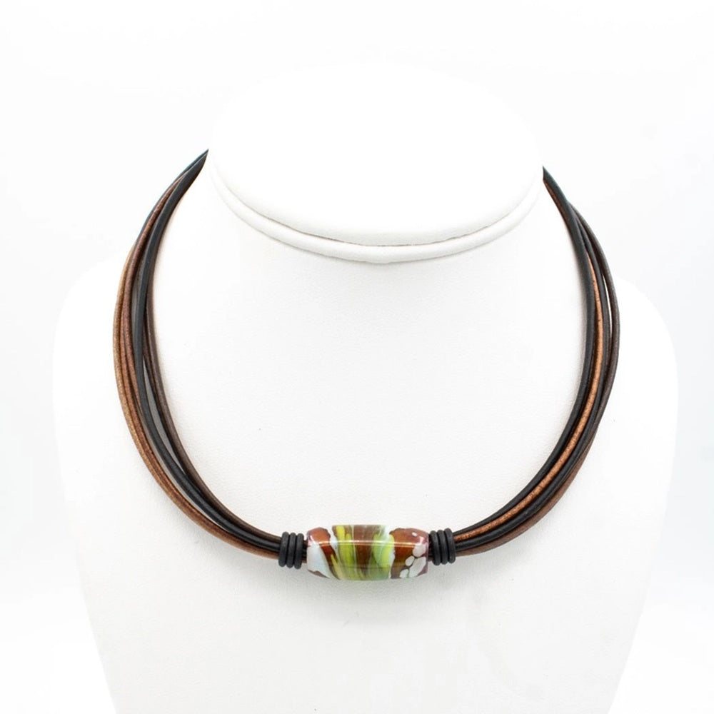 A multi-strand cord necklace with dark brown and reddish-brown cords, featuring a central glass lampwork bead with green, white, and brown marbled patterns, displayed on a white mannequin bust.