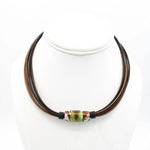 A multi-strand cord necklace with dark brown and reddish-brown cords, featuring a central glass lampwork bead with green, white, and brown marbled patterns, displayed on a white mannequin bust.