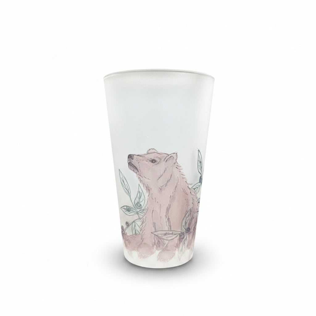 A frosted glass tumbler featuring a hand-drawn illustration of a brown bear surrounded by blue leaves, set on a white surface