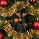 Decorative ornament of a bear holding an orange ball on a Christmas tree with gold tinsel and red ornaments.