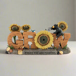 Decorative sign with 'GROW' letters surrounded by sunflowers and a bear figurine on a white background.