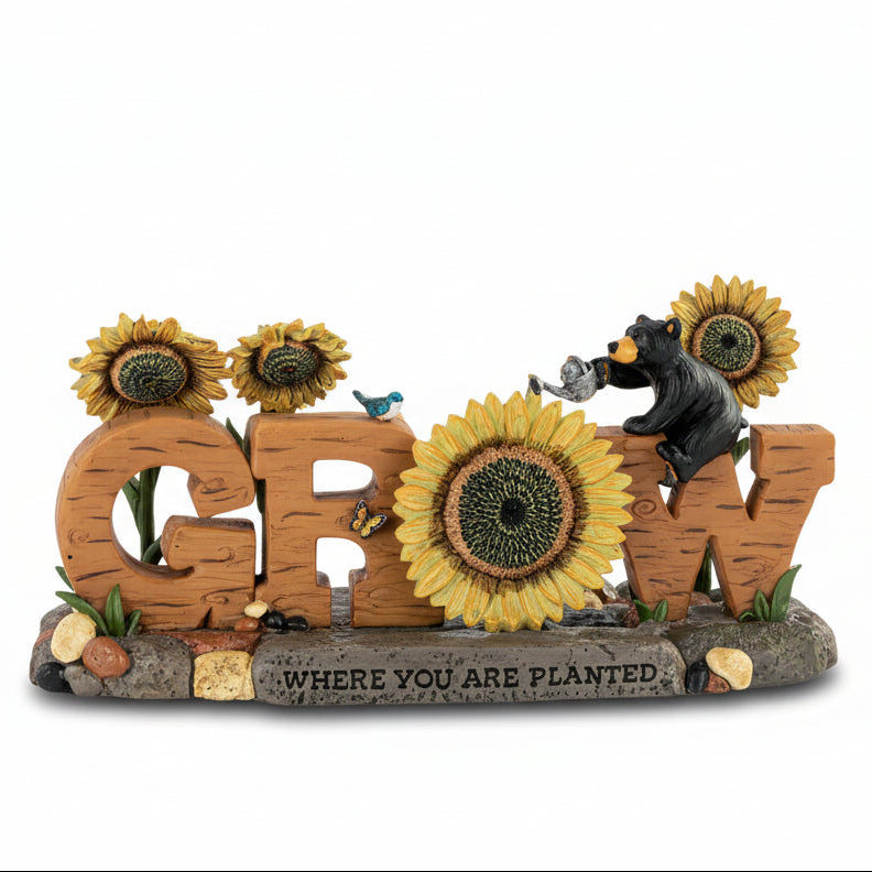Decorative sign with 'GROW' letters surrounded by sunflowers and a bear figurine on a white background.