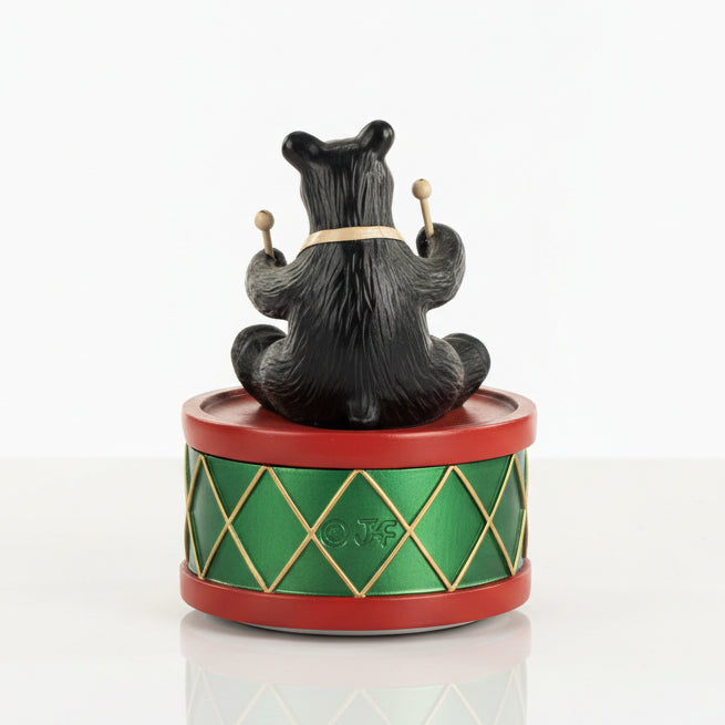 Black bear figurine on a green and red drum with gold accents on a white background