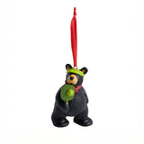Black bear ornament with green hat and pickleball paddle, hanging from a red string on a white background