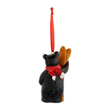 Decorative bear ornament with a red bow and wooden utensils on a white background