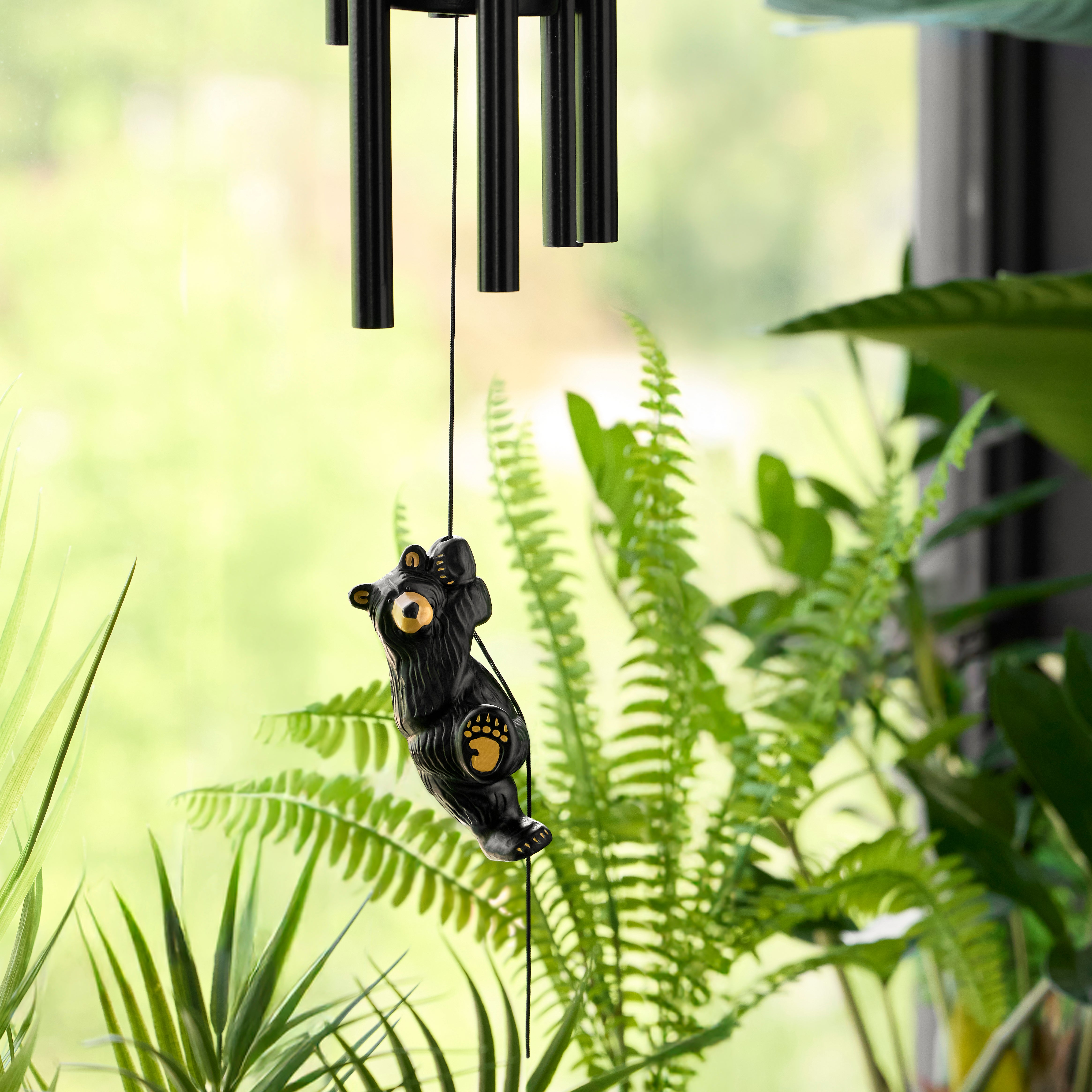 Black bear-shaped wind chime hanging among green plants
