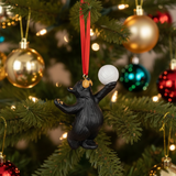 Black bear ornament holding a white ball on a Christmas tree with colorful ornaments.