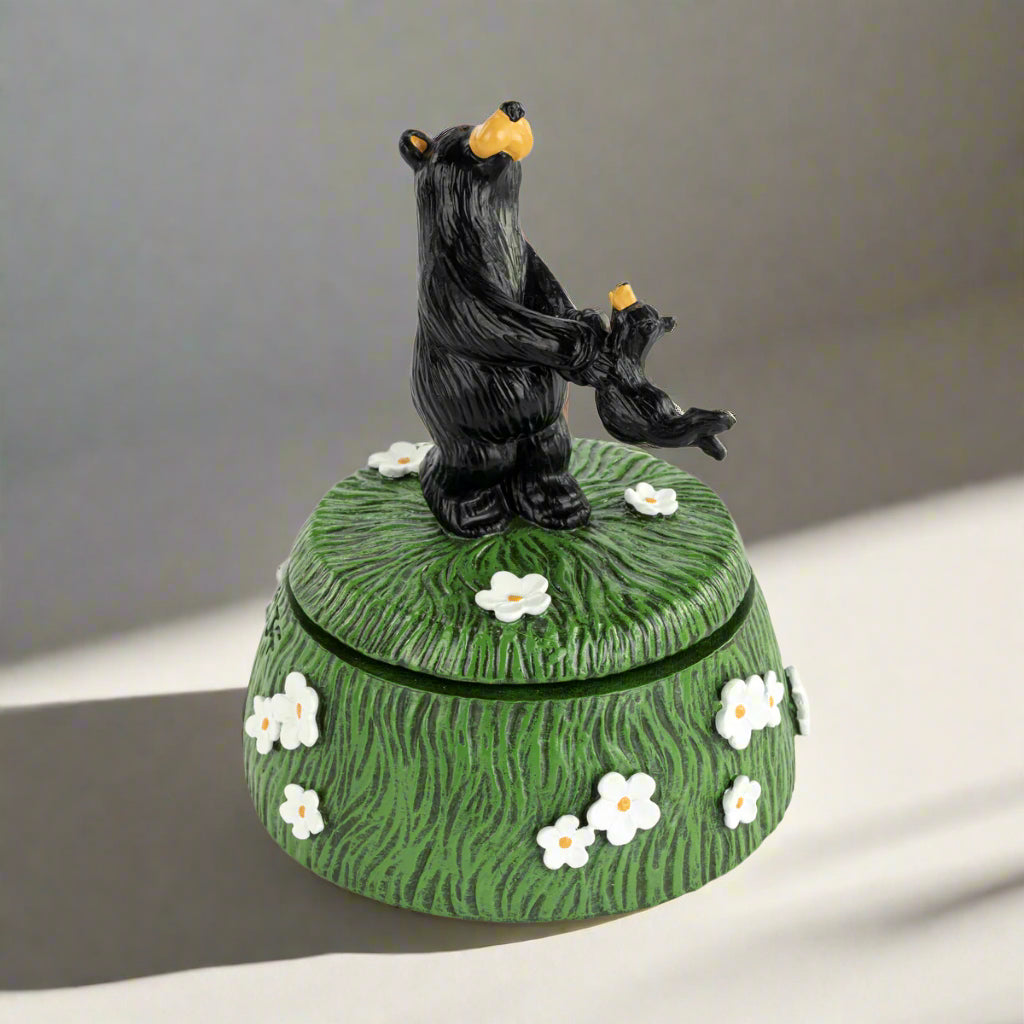 Decorative box with a black bear figurine on top, featuring white flowers on a green background.