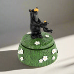 Decorative box with a black bear figurine on top, featuring white flowers on a green background.
