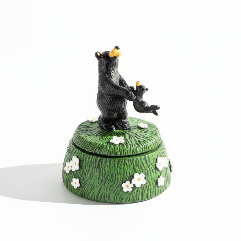 Decorative box with a black bear figurine on top, featuring white flowers on a green background.