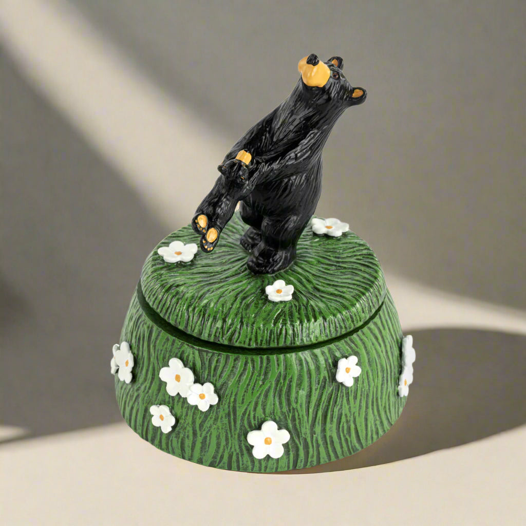 Decorative box with a black bear on top, surrounded by flowers on a white background